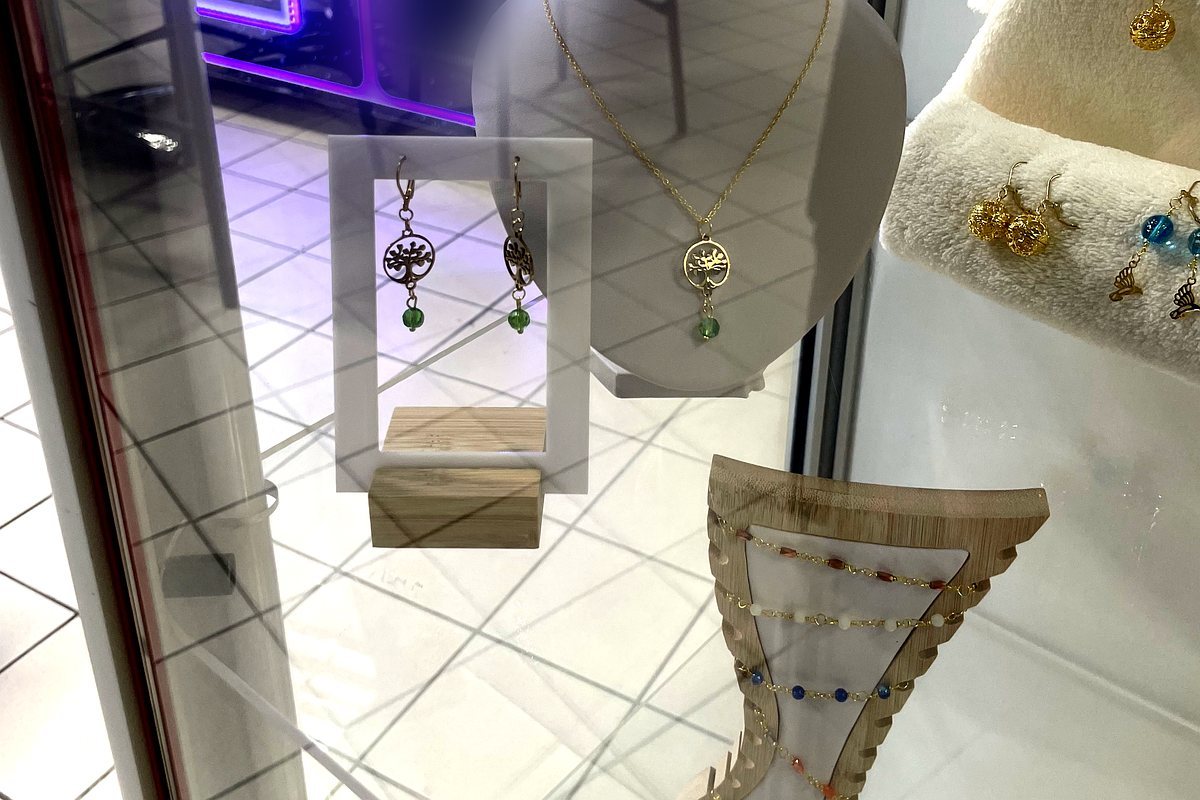 Vue des vitrines en galerie marchande : présentoirs bustes blancs et noirs, colliers et parures disposés derrière le verre, sur fond de sol carrelé clair.
