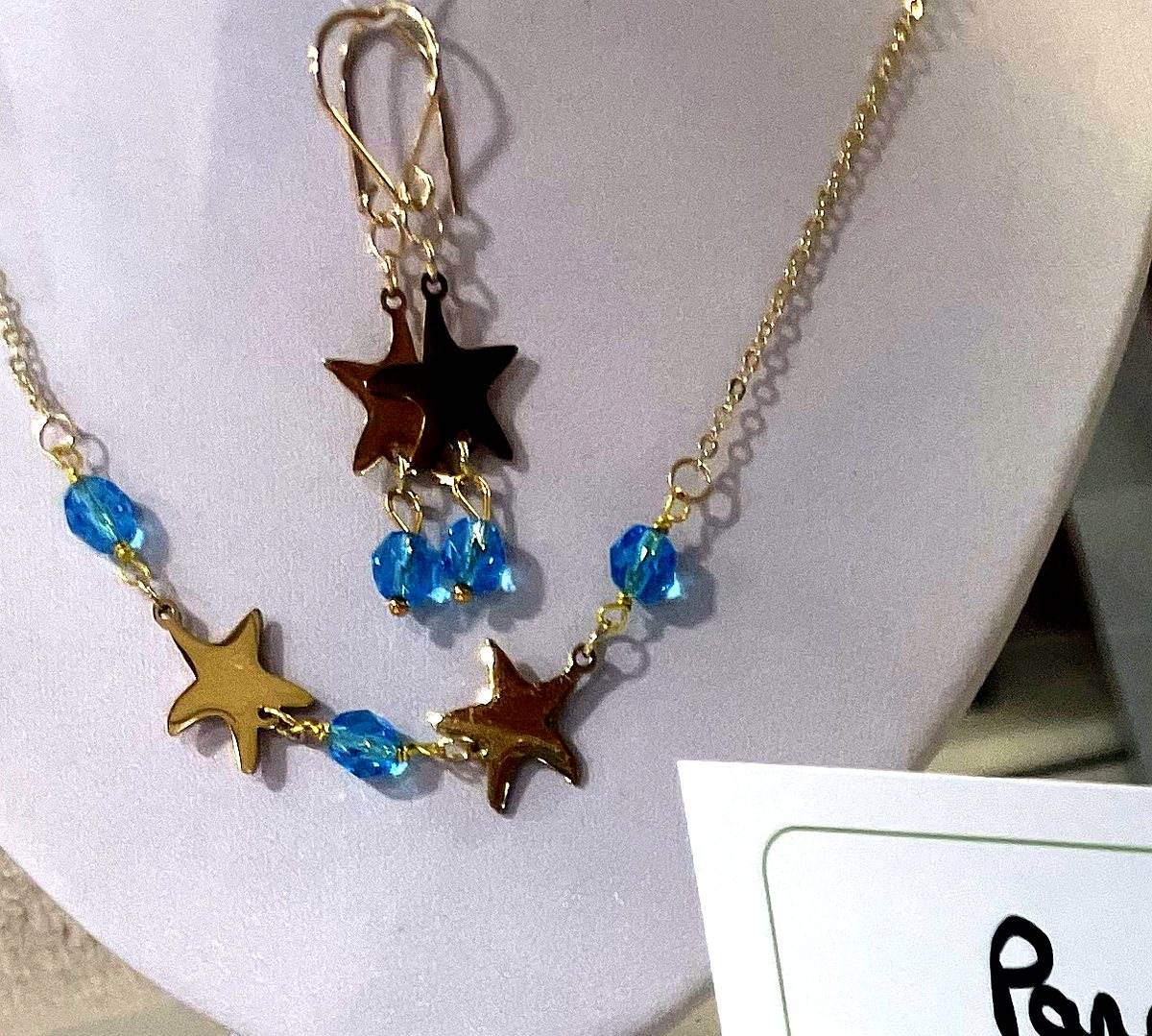 Parure faite main : collier et boucles d’oreilles assortis, étoiles dorées et perles de verre bleu turquoise facettées sur une chaîne dorée fine.