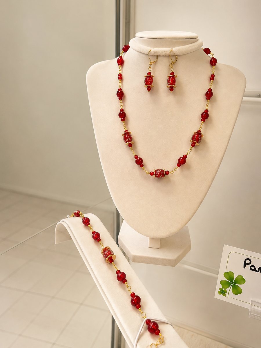 Parure rouge faite main en trois pièces : collier long de perles rouges facettées alternées de grosses perles filigranées dorées, boucles d’oreilles assorties et bracelet coordonné.