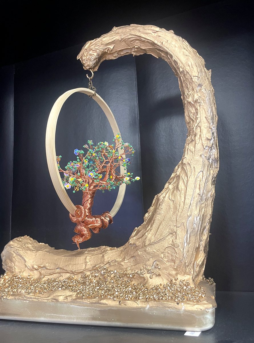 Sculpture faite main : arbre miniature en fil de cuivre torsadé au feuillage de perles vertes et de petites fleurs, suspendu par une chaînette dans un cercle de bambou, accroché à une vague de plâtre moulé et doré, en relief sur un socle de plâtre.